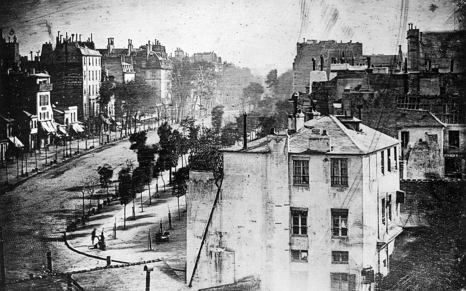 Old daguerreotype of a tree-lined boulevard flanked by rooftops and multistory buildings