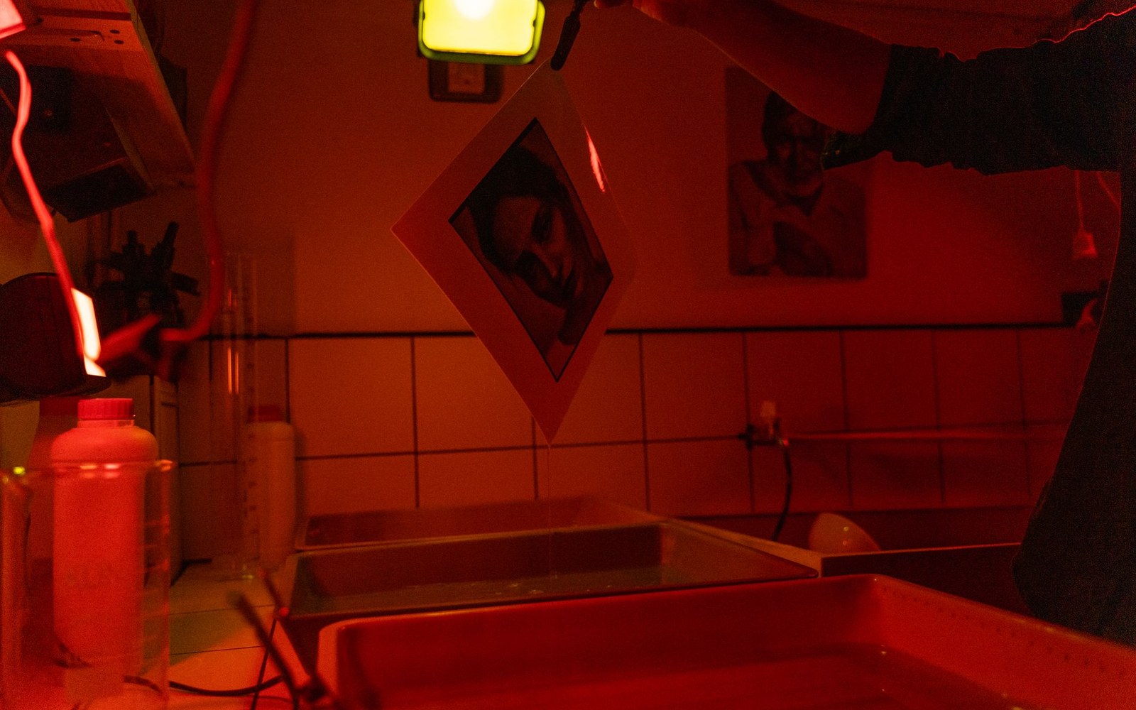 A darkroom lit red, with a hanging photo print and developing trays below